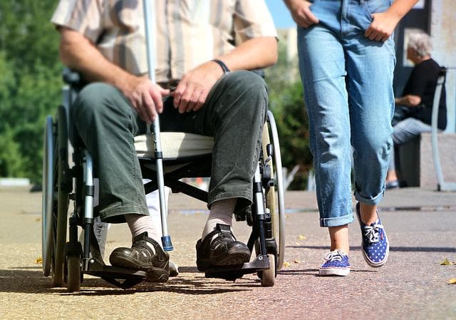 Accompagnement d’une personne en situation de handicap, main posée sur la roue d’un fauteuil roulant